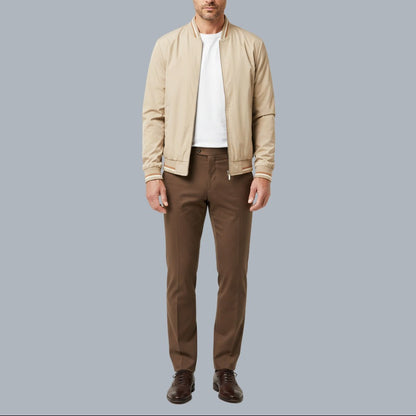 Man wearing a beige jacket, white shirt, and brown pants on a gray background